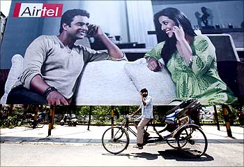 A rickshaw driver talks on his mobile phone as he rides past a billboard.