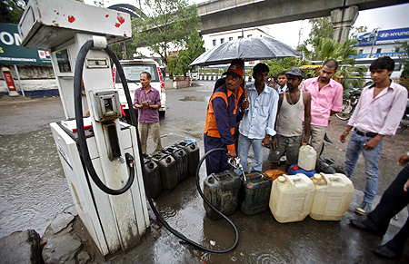 A worker fills diesel in containers at a fuel station during a rain shower at Noida.