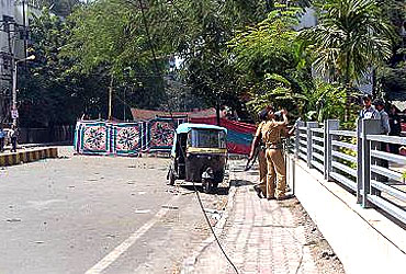 An autorickshaw lies abandoned a few feet away from German Bakery as cops who have been on duty for more than 15 hours at a stretch drink water