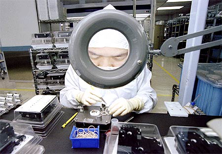 An employee of Seagate Technology is enlarged by a magnifying glass as she concentrates on assembling hard disk drives at their Singapore plant.