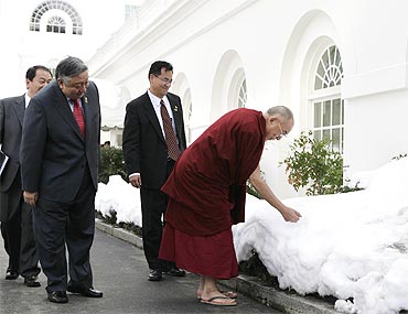 The Dalai Lama touches the snow as he walks outside the White House