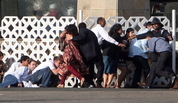 People duck for cover as gunshots are fired from inside Hotel Taj Mahal during the 26/11 terror attacks in Mumbai